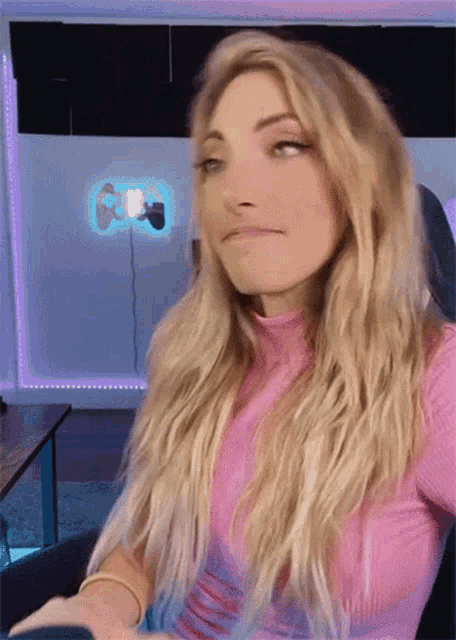 a woman in a pink shirt is sitting in front of a neon sign that says ' nintendo ' on it .