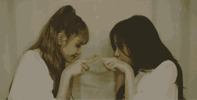 two girls are making a heart shape with their fingers