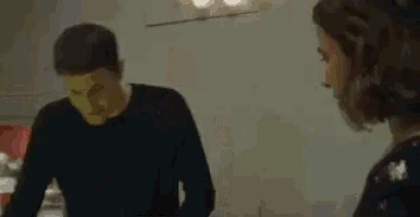 a man with a green mask on his face is talking to a woman in a kitchen .