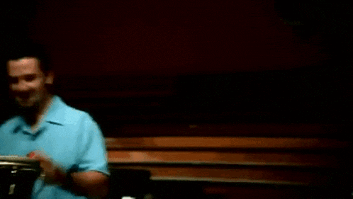 a man in a blue shirt is eating a banana in front of drums