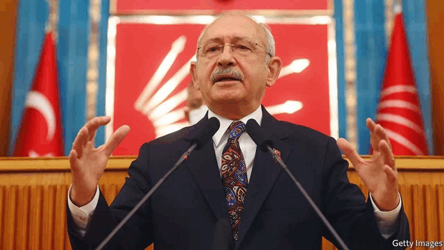 a man in a suit and tie is giving a speech in front of microphones