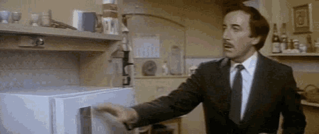 a man in a suit and tie is reaching into a refrigerator in a kitchen .