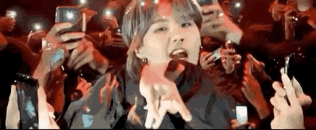 a woman is singing into a microphone in front of a crowd of people holding their phones .