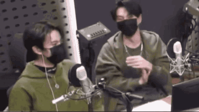two men wearing masks are sitting in front of microphones .