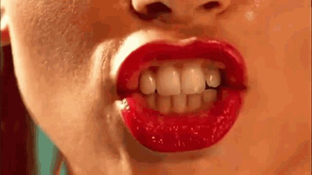 a close up of a woman 's mouth with red lipstick and white teeth making a funny face .