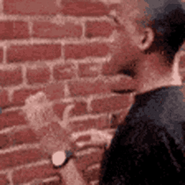 a man is standing in front of a brick wall and looking at his watch .