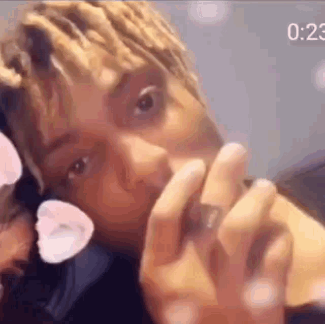 a close up of a person 's face with a flower in their hair and a ring on their finger .