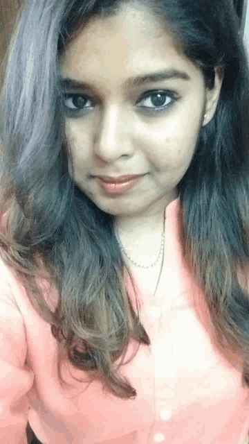 a woman wearing a pink shirt and a necklace looks at the camera