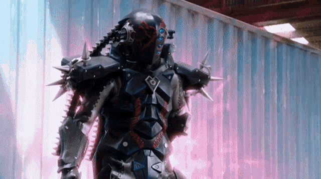 a robot with spikes on it 's arms and legs stands in front of a pink wall