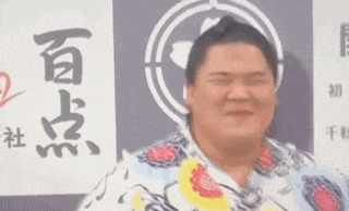a man with a bun on his head is crying in front of a wall with chinese writing on it .