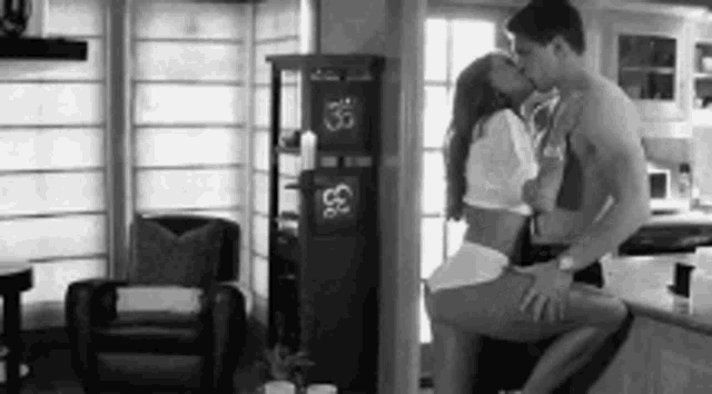 a man and a woman are kissing in a kitchen .