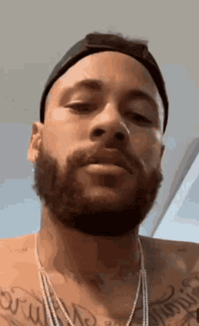 a man with a beard and a hat is wearing a necklace and earrings .