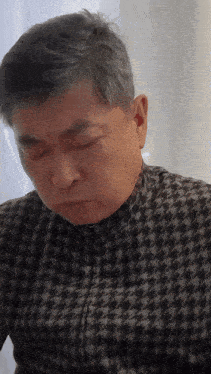 a man with gray hair is wearing a black and grey shirt
