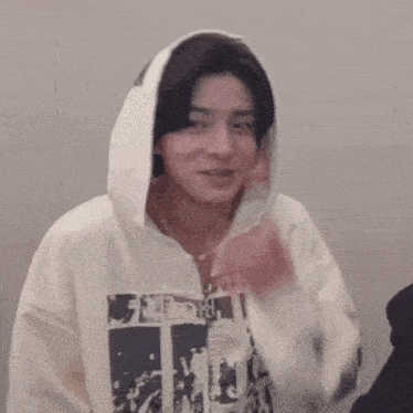 a young man wearing a white hoodie is covering his mouth with his hand .