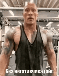 a man in a black tank top is standing in a gym with a tattoo on his arm .
