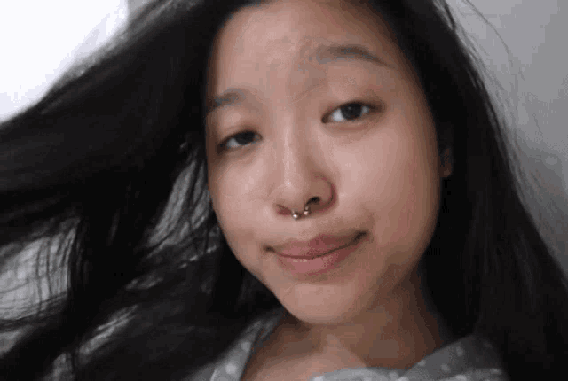 a woman with a nose ring is smiling and her hair is blowing in the wind