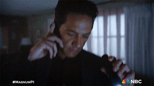 a man is holding a flashlight and talking on a cell phone with a nbc logo in the background