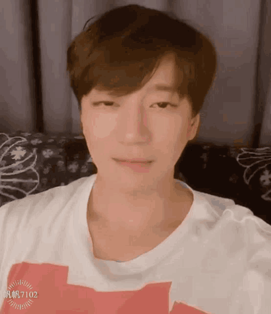 a young man is sitting on a couch wearing a white t-shirt with a red and white cross on it .