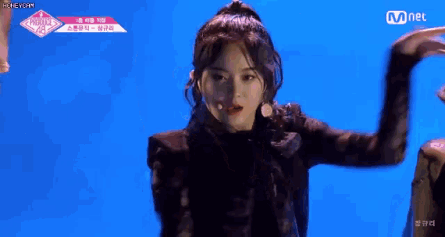 a woman is dancing on a stage in front of a blue background with mnet written on the bottom