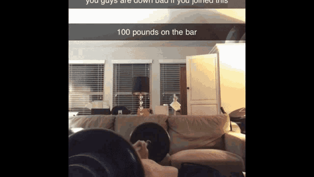 a man is lifting a barbell in a living room with the words 100 pounds on the bar above him