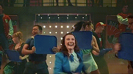 a woman in a blue shirt is dancing in front of a sign that says wg on it