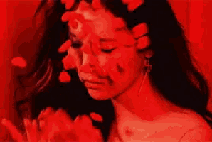 a close up of a woman 's face with red petals in her hair