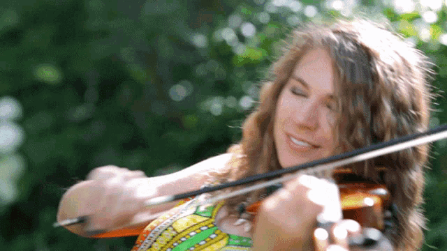 a woman playing a violin with her eyes closed and smiling