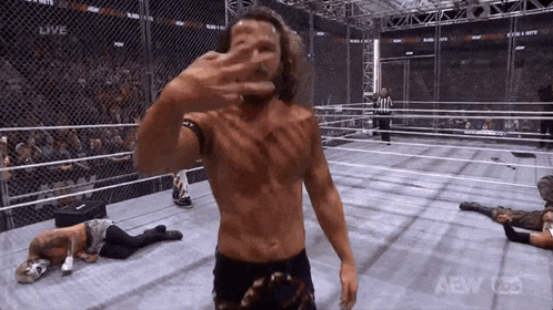 a man without a shirt is standing in a wrestling ring covering his face with his hand .