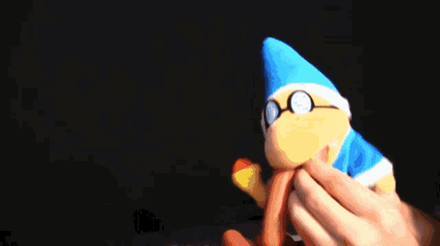 a person is holding a stuffed animal with a blue hat and glasses on it .