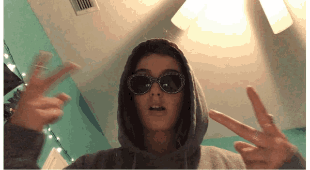 a girl wearing sunglasses and a hoodie is giving the peace sign