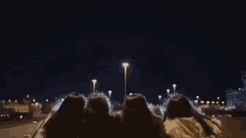 a group of people are sitting in a car watching fireworks at night .