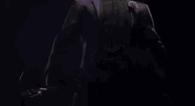 the joker is smiling in the dark and wearing a purple suit .