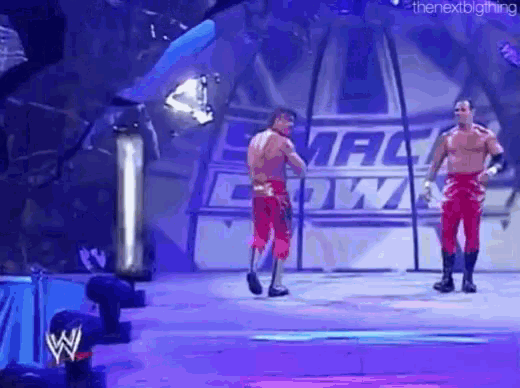 two wrestlers are standing on a stage in front of a sign that says ' smackdown ' on it .