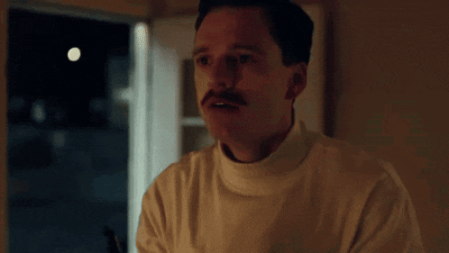 a man with a mustache holds a gun in his hand