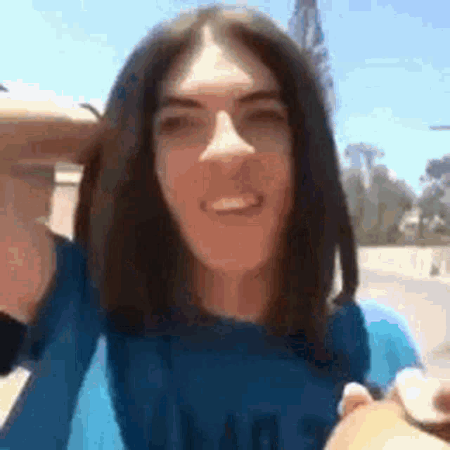 a woman with long hair and a blue shirt is holding a sandwich and smiling .