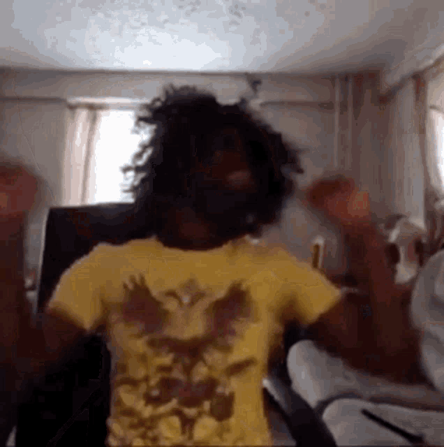 a man with curly hair is dancing in a living room while wearing a yellow shirt .