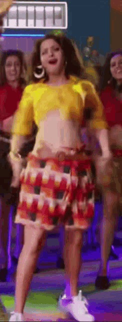 a woman in a yellow top and a colorful skirt is dancing on a dance floor .