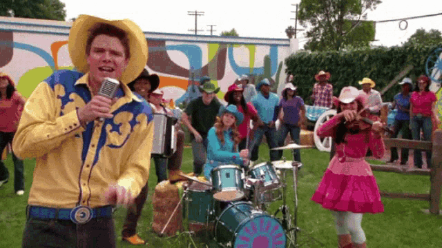 a man in a cowboy outfit sings into a microphone in front of a drum set