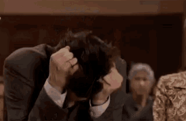 a man in a suit and tie is covering his face with his hands while sitting in a courtroom .