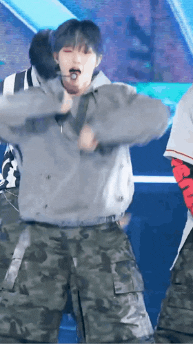 a man in a gray hoodie and camouflage pants is dancing on a stage .