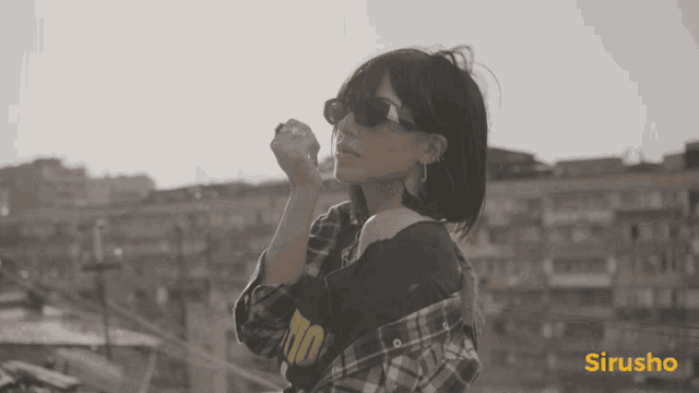 a woman wearing sunglasses and a plaid shirt is standing in front of a yellow sign that says sirisho