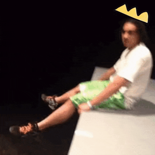 a man wearing a crown is sitting on a wall with his legs crossed