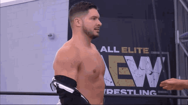 a shirtless wrestler is standing in front of a sign that says all elite wrestling