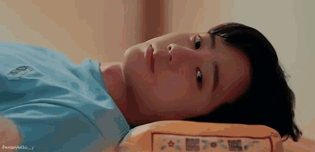a young boy is laying on a bed with a yellow pillow and a blue shirt .