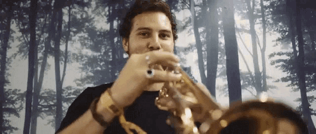 a man in a black shirt is playing a trumpet in front of a forest background .
