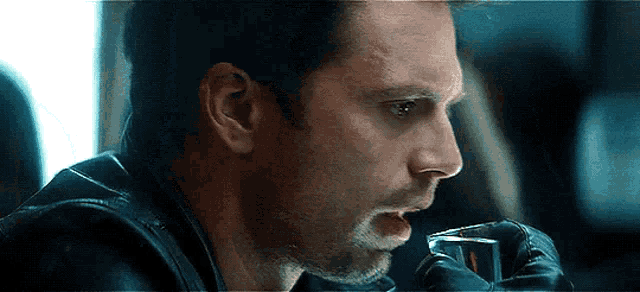 a man in a leather jacket is drinking from a shot glass with his mouth open .
