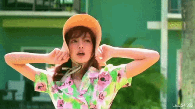a woman wearing a straw hat and a floral shirt is covering her ears .