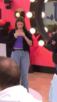 a woman in a purple top and blue jeans is standing in front of a large mirror