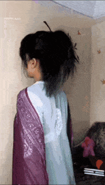 a woman wearing a purple shawl and a blue shirt is standing in front of a wall .