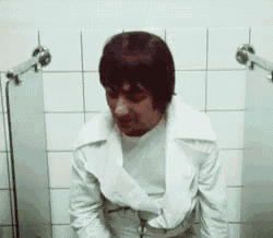 a man in a white jacket is sitting on a toilet in a bathroom .